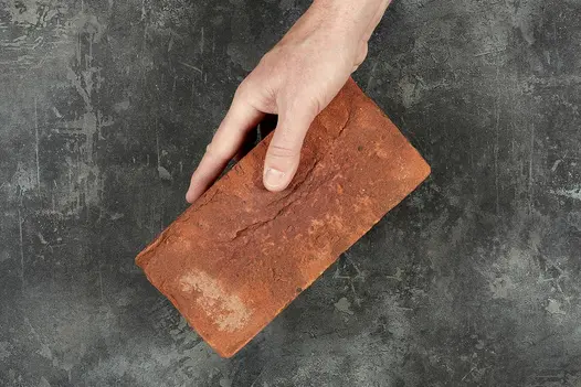 Hand holds one single romsey antique clay paver over a black background to show off the belgian bricks colour and texture.