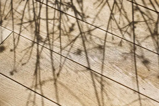 Close-up of Golden Oak Millboard wood-free Decking boards, showing variations in grain, with shadows of plants falling across them.