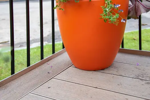 Bottom of large orange pot on Warm Teak Grooved DesignBoard, black railings behind, on Balcony Garden built by Big Fish Landscapes.