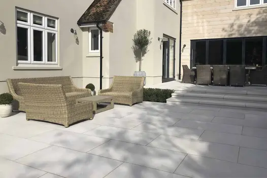 Comblanchien porcelain patio with wide garden steps leading to ratan garden furniture set located in front of bifold doors.