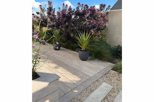 Pebble and plank path leads to cinnamon designboard composite decking that has flowerpots lining the course.