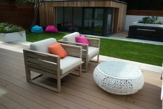 2 rattan armchairs and coffee table sit on mocha designboard composite decking and lawn adjacent with outhouse in the background.