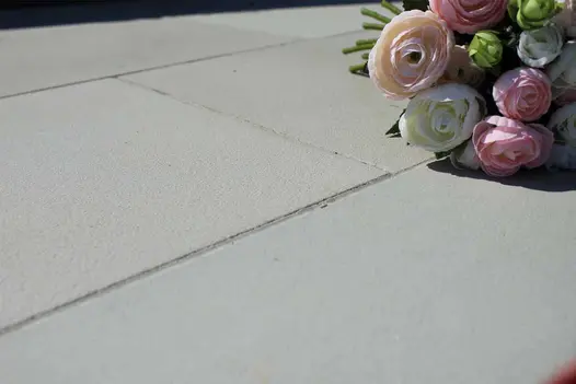 Close-up of Contemporary Grey sandstone smooth paving slabs, showing colour and sandblasted finish, with rose bouquet in background.