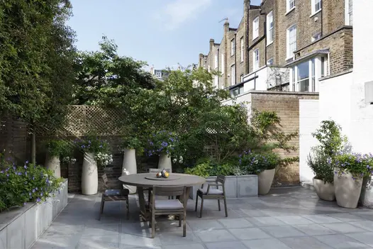Tall white pots and square planters line edge of Contemporary Grey sawn sandstone patio laid between raised bed and house wall.