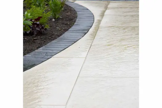 Close up shot showing texture in wet weather of Golden Stone Porcelain Paving cut into curves around a flowerbed.