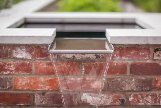 Water pours from raised pond with flat spout at top of wall with Jura grey limestone coping. Design by Simon Orchard.