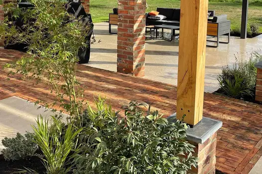 Close up shot through flowerbed and pergola showcase cotswold clay paver bricks with garden furniture in the background.