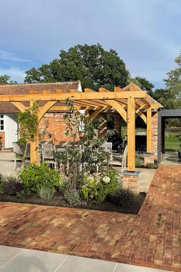 Freshly dug flowerbeds next to an L shaped path of Cotswold Clay paver bricks beneath wooden pergola.