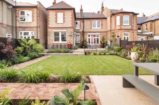 Cotswold clay paver path, between lawn and long border with architectural plants, leads from patio to brick-paved area with beds.