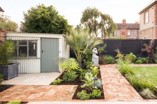Garden designed by Kiwi landscapes, with white shed, modern figurative sculpture on plinth, and path of Cotswold clay pavers.