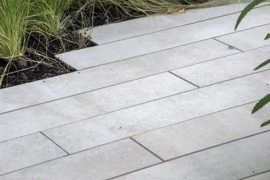 Cream porcelain planks, laid running bond, creating jagged edging to bed planted with grasses by James Smith. Built by Topoforma.