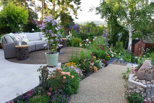 Raised garden terrace featuring circular composite decking, Cream porcelain patio and resin bound gravel path broken up with vibrant planting.