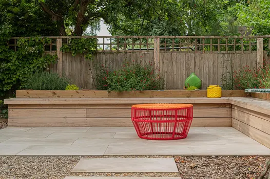 Back garden L shaped bench constructed from hard wood timber sitting on top of a Cream porcelain paving patio.