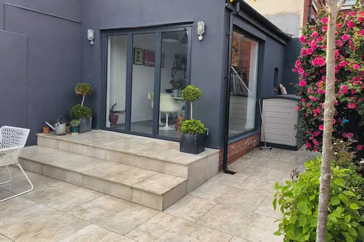 Grey kitchen extension with bi fold doors stepping down onto a Cream porcelain paved patio grouted with buff coloured grout.