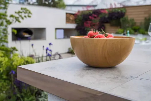 Wooden bowl full of tomatoes sits on countertop laid with Jura Grey smooth limestone slabs with very narrow joints.