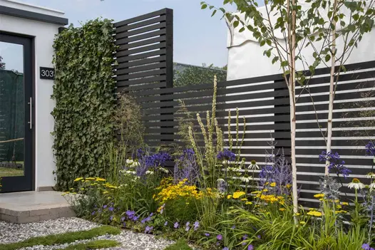 Tall open-slatted screens of Dark Ash composite wood battens form boundary of RHS show garden behind colourful planted border.