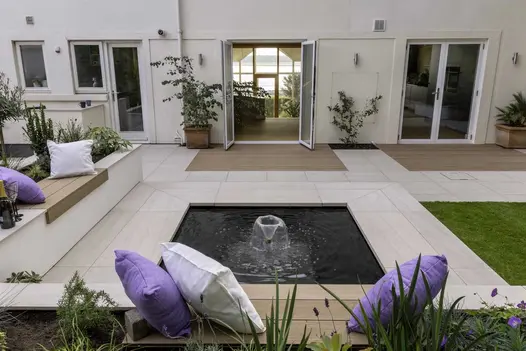 Patio of Faro Porcelain slabs with square pond edged. Raised beds topped with matching coping and Mocha composite decking boards.