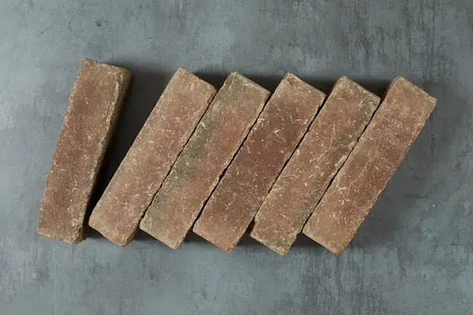 6 Derby Dutch clay pavers laid at a slant on grey background, showing brown tones, white flecks and tumbled edges. 