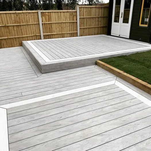 Raised deck of luna designboard composite decking leads from building to lower deck, to lawn area, wooden fencing in the background.
