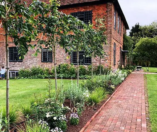 Red brick house with large lawn sits next to small path of dorset antique clay pavers with young trees running alongside.