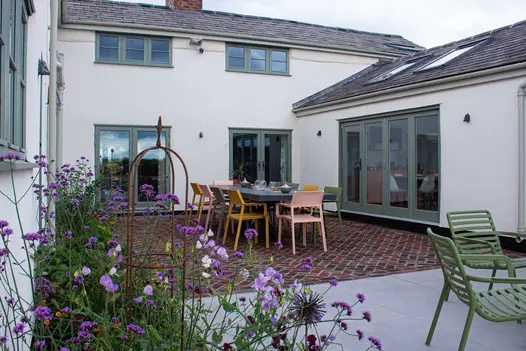 Dining set in courtyard of white house paved with Dorset Antique Belgian bricks laid in zigzag pattern. Design by Urban Landscapes.
