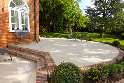 Circle patio of light paving against red brick house, flanked by Dorset Antique Belgian Bricks, pavers also used as steps.
