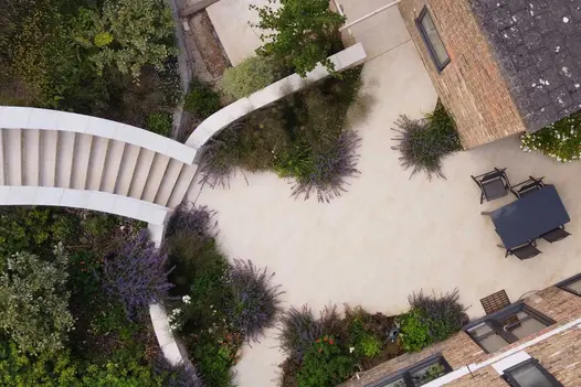 Looking directly down onto a Golden Stone Porcelain patio dining area with adjoing gently curving steps and a table and chairs.
