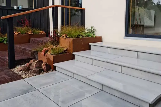 3 Dove grey bullnose sawn sandstone steps with matching risers, next to 2 corten steel troughs below sliding patio doors.