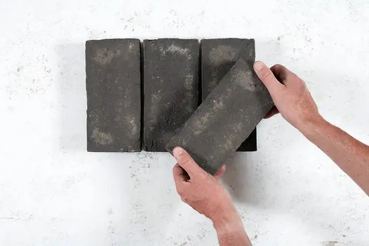 2 hands put a paver at angle on top of 3 Durham Clay Paver Bricks, showing texture and grey and white tones. Available nationwide.