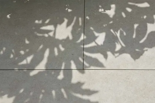 Dappled sunlight falls across Egyptian Beige Porcelain Paving, highlighting the soft texture and pale finish of the slabs.
