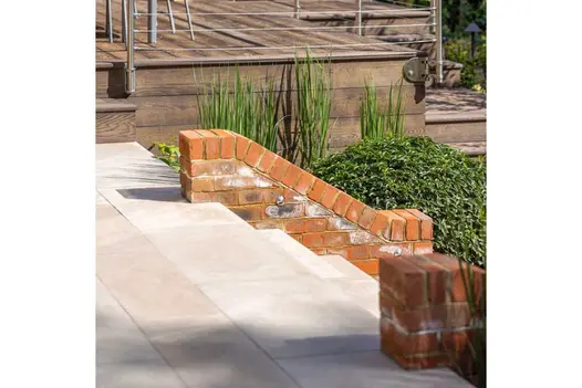 Egyptian Beige smooth limestone steps rise between brick flank walls to matching paved area with raised decking in background.