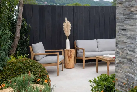 Egyptian Beige Smooth Limestone paves seating area next to beds. Composite planks form fence behind wooden outdoor lounge set.