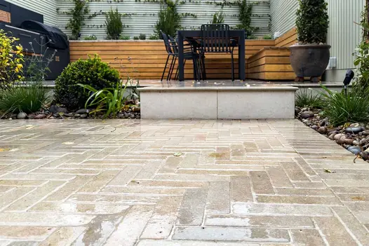 Egyptian Beige Limestone pavers in a wet finish, laid in a herringbone pattern beside raised step and garden planting.