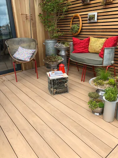 two metal chairs sit on mocha designboard decking surrounded by potted plants and plants hanging off the wall.