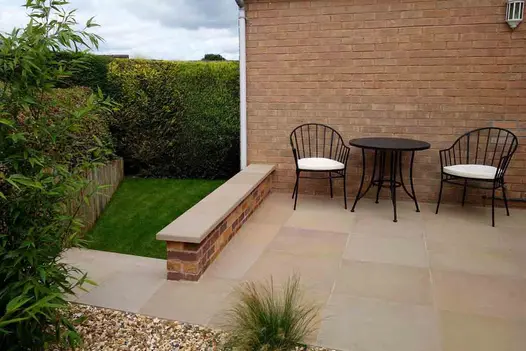2 chairs and table on patio next to wall of house and low brick parapet topped with Buff sawn sandstone coping to match paving.