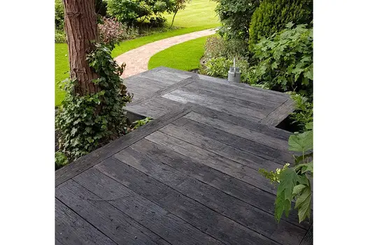 3 square platforms of Embered Millboard decking descend between tree and thick bushes to sinuous clay paver path set into grass.
