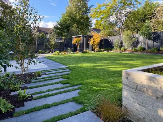 Staggered Black Granite plank paving slabs set into lawn with grass joints, leads to paved area. Pergola in background.