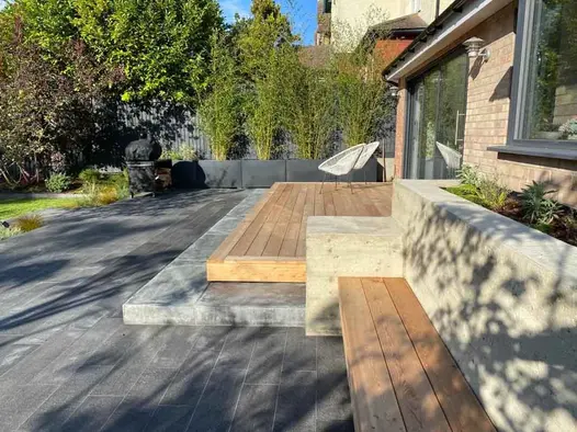 Patio of Black granite plank paving across back of house, with 2 steps up to wooden deck outside bi-fold doors.