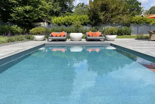 Cinder porcelain 40mm bullnose step treads used as coping of rectangular swimming pool set into large patio of fenced garden.