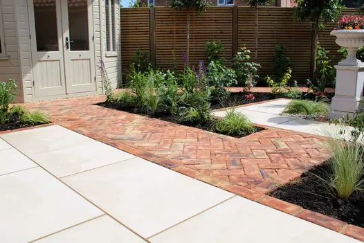 Garden house with patio of cream paving and Cotswold clay pavers laid herringbone with inset beds. Built by Essex Garden Designs.