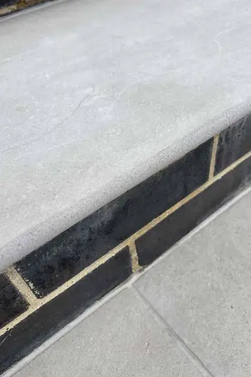 Close up of the bullnose of Florence Grey 20mm Moulded off the shelf Step next to black bricks, showing texture.