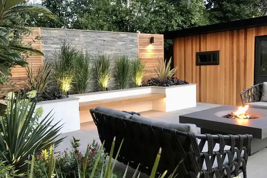 2-seater sofa by stone fire table, in front of feature wall with raised bed under cedar and Graphite sandstone cladding panels.