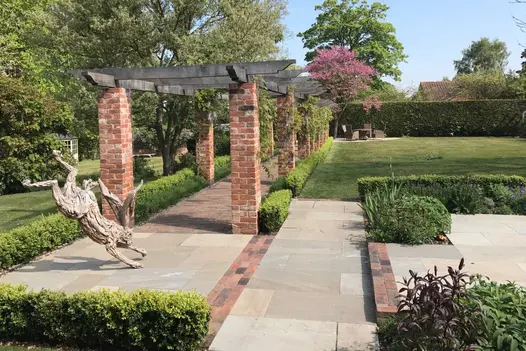 Wooden hare sculpture on paving with Romsey Antique clay bricks detailing at end of colonnade of brick pillars next to lawn.