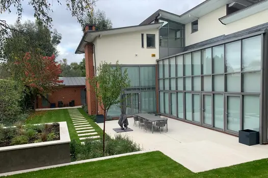 Contemporary house with tall windows and doors leading to patio paved with Faro porcelain paving and furniture 8-seat dining set.