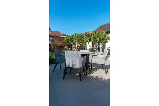 Rattan garden furniture set positioned on light coloured porcelain tiles with two medium-sized trees showing in the background.