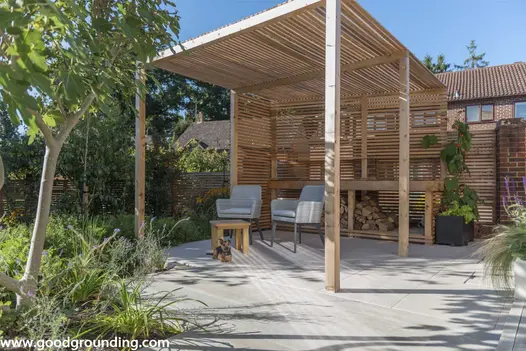 Faro porcelain paving laid under wooden pergola that covers two garden chairs and a coffee table, ideal for relaxing outdoors.