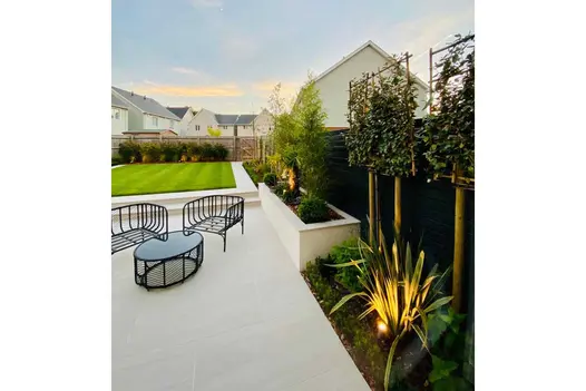 Black outdoor furniture on Faro Porcelain Paving patio with plant border. 2 steps up to lawn beyond. By Landscape Design Studio.