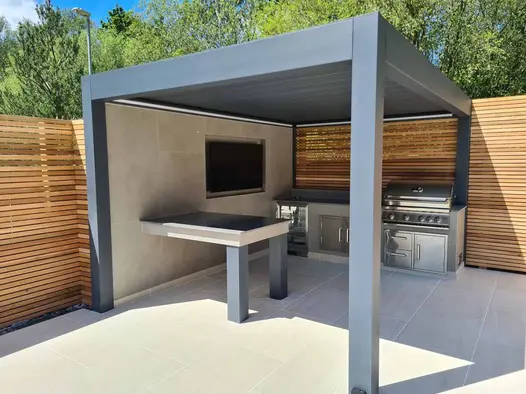 Metal Pergola Louvered Roof positioned over outdoor cooking area with bbq and fridge with DesignClad wall cladding featuring a tv.