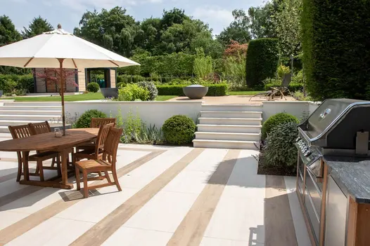 Outdoor cooking space on Faro porcelain patio, wooden garden furniture and porcelain steps to the side leading to relaxation area.