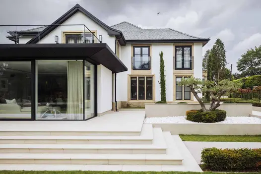 Large white house surrounded with wraparound Faro porcelain patio on all sides, with 5 steps descending to lawn. 